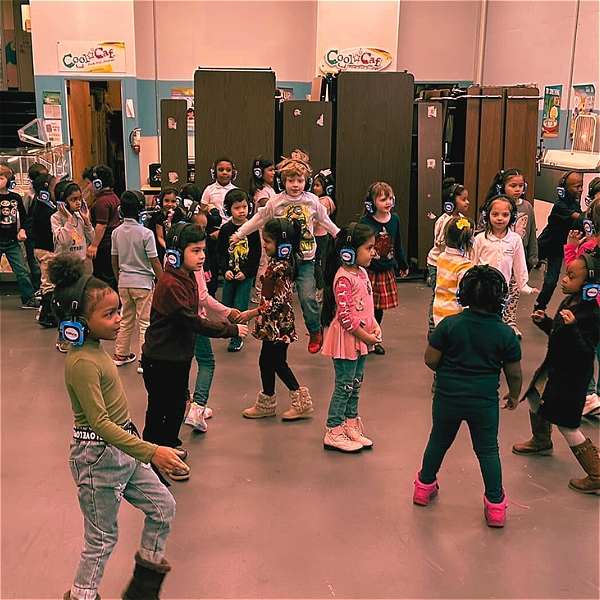 This is a photo of young children in a room. Each of the children are wearing a headset, and they are dancing in a silent disco.