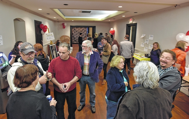 A photo of about 15 to 20 people in a room with very little ornamentation on the walls. Most of the people are in small groups talking to each other.