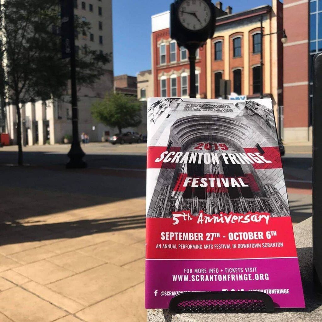 A close-up photo of the 2019 Scranton fringe Festival fifth anniversary program. It is sitting on a ledge in a downtown Square.